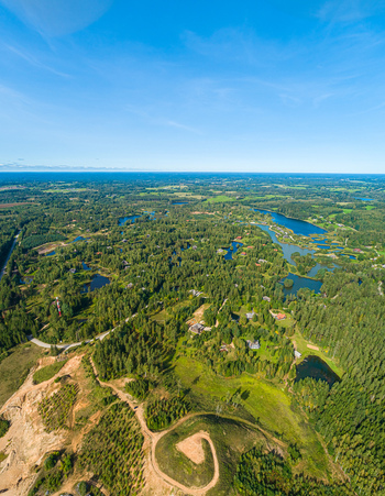 Aerial view of a lush forest landscape in Latvia featuring winding dirt paths scattered small lakes and dense green trees under a clear blue sky Latvia. Aerial view of a lush forest landscape in Latvia featuring winding dirt paths scattered small lakes and dense green trees under a clear blue sky Latvia.