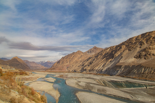View of a river winding through a stark mountainous landscape under a sky brushed with delicate clouds Skardu Gilgit Baltistan Pakistan.