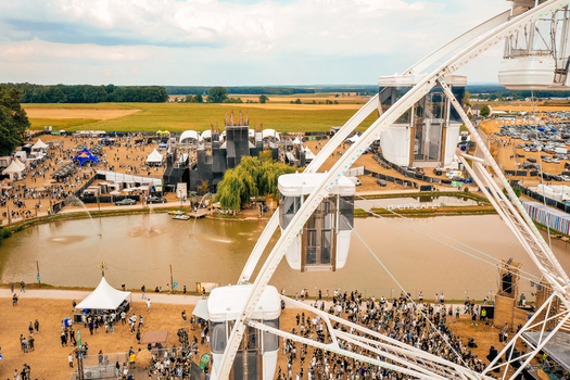 Herzogenaurach Germany 22 July 2022 Aerial view of the Open Beatz Festival with a large white ferris wheel in the foreground and crowds gathered near the main stage and fields. Herzogenaurach Germany 22 July 2022 Aerial view of the Open Beatz Festival with a large white ferris wheel in the foreground and crowds gathered near the main stage and fields.