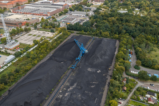 Aerial view of coal storage area with large black piles a blue crane and industrial facilities surrounded by trees in Berlin Berlin Germany.