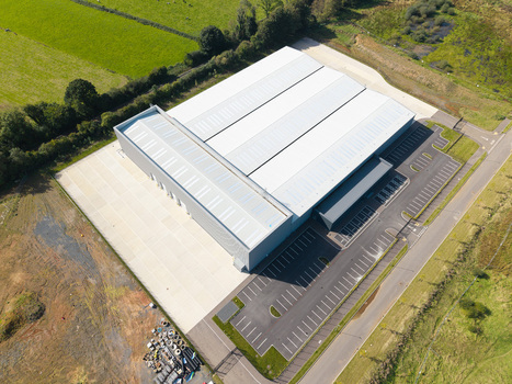 Aerial view of a large modern industrial warehouse building with a spacious parking lot surrounded by green fields in Lisburn Northern Ireland United Kingdom. Aerial view of a large modern industrial warehouse building with a spacious parking lot surrounded by green fields in Lisburn Northern Ireland United Kingdom.