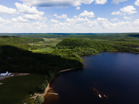 Aerial view of Commanda Lake surrounded by dense green forests and rolling hills under a bright blue sky with scattered white clouds in Restoule Ontario Canada. Aerial view of Commanda Lake surrounded by dense green forests and rolling hills under a bright blue sky with scattered white clouds in Restoule Ontario Canada.