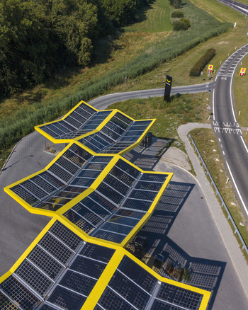Aerial view of the Fastned charging station with its distinctive yellow zigzag solar roof structure situated near a road junction in Lelystad Flevoland Netherlands. Aerial view of the Fastned charging station with its distinctive yellow zigzag solar roof structure situated near a road junction in Lelystad Flevoland Netherlands.