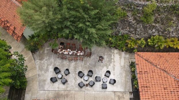 Aerial view of a courtyard with outdoor dining tables chairs and lush trees in Tanjungsari Special Region of Yogyakarta Indonesia. Aerial view of a courtyard with outdoor dining tables chairs and lush trees in Tanjungsari Special Region of Yogyakarta Indonesia.