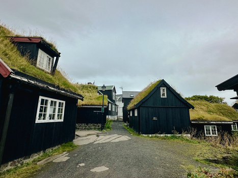 View of traditional black wooden houses with grass roofs lining a narrow gravel path in the Faroe Islands. View of traditional black wooden houses with grass roofs lining a narrow gravel path in the Faroe Islands.