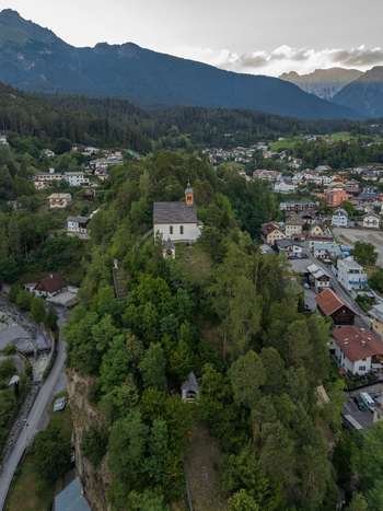 Aerial view of St. Laurentius Church perched on a forested hill overlooking the town of Imst with the surrounding Alpine landscape. Imst Tyrol Austria.