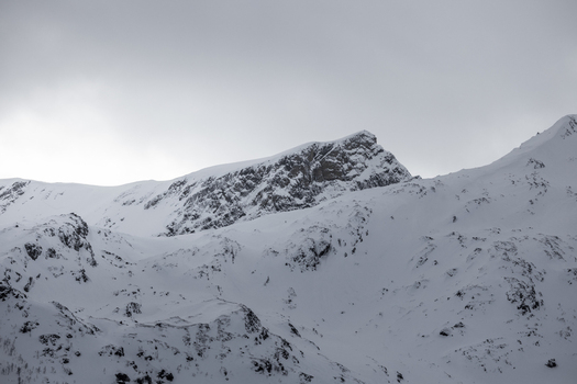View of snow covered mountain peaks and rugged slopes under an overcast winter sky in Ersfjord Troms Norway. View of snow covered mountain peaks and rugged slopes under an overcast winter sky in Ersfjord Troms Norway.