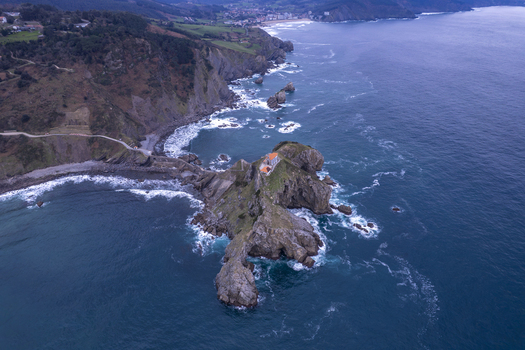 Aerial view of San Juan de Gaztelugatxe a historic hermitage on a rocky islet with a winding stone bridge surrounded by the deep blue Bay of Biscay Gaztelugatxeko Doniene Euskadi Spain.