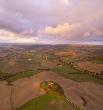 Aerial view of the rolling hills of the Crete Senesi landscape near Asciano featuring golden hour light soft clouds and agricultural fields in Asciano Tuscany Italy.