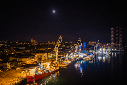 Aerial view of the illuminated Uljanik shipyard at night with industrial cranes docked ships and city lights along the waterfront in Pula Istria County Croatia. Aerial view of the illuminated Uljanik shipyard at night with industrial cranes docked ships and city lights along the waterfront in Pula Istria County Croatia.