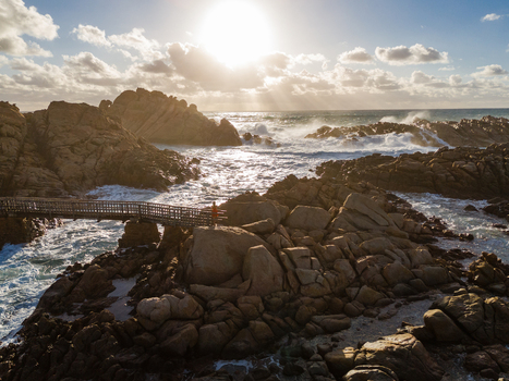 Aerial view of Canal Rocks Bridge with a person on the walkway amidst rugged granite rocks and crashing waves under a bright sun in Yallingup Western Australia Australia. Aerial view of Canal Rocks Bridge with a person on the walkway amidst rugged granite rocks and crashing waves under a bright sun in Yallingup Western Australia Australia.