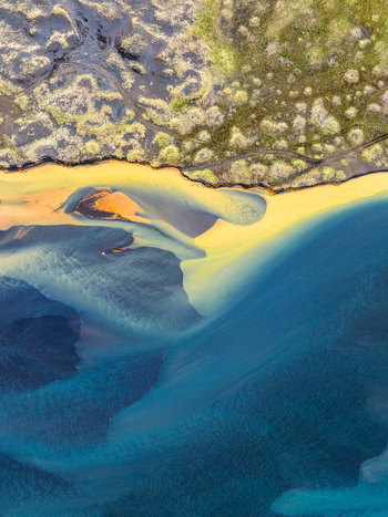 Aerial view of a glacial river delta with intricate patterns of sediment rich blue and yellow water flowing through dark volcanic terrain in Iceland. Aerial view of a glacial river delta with intricate patterns of sediment rich blue and yellow water flowing through dark volcanic terrain in Iceland.