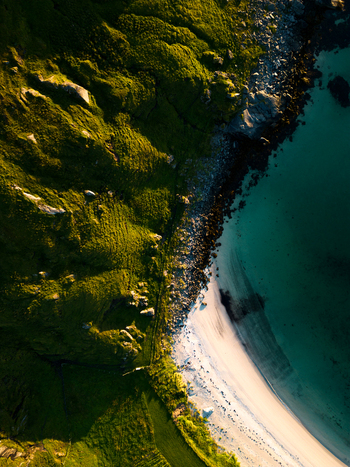 Aerial view of the rugged coastline with green grassy hills a rocky shore and a white sandy beach meeting turquoise water in Leknes Nordland Norway. Aerial view of the rugged coastline with green grassy hills a rocky shore and a white sandy beach meeting turquoise water in Leknes Nordland Norway.