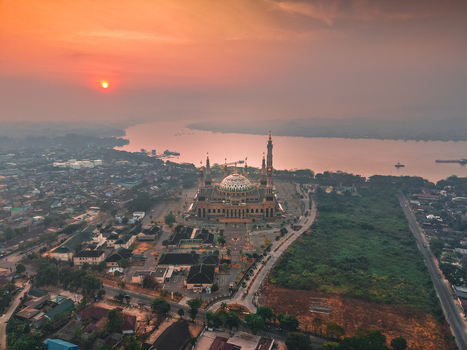 Aerial view of Baitul Muttaqien Mosque at sunset situated along the Mahakam River with surrounding urban landscape in Samarinda East Kalimantan Indonesia.