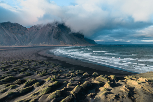 Aerial view of Vestrahorn mountain rising above the dramatic black sand beach and grassy dunes under a cloudy sky Sveitarfelagid Hornafjordur Iceland. Aerial view of Vestrahorn mountain rising above the dramatic black sand beach and grassy dunes under a cloudy sky Sveitarfelagid Hornafjordur Iceland.