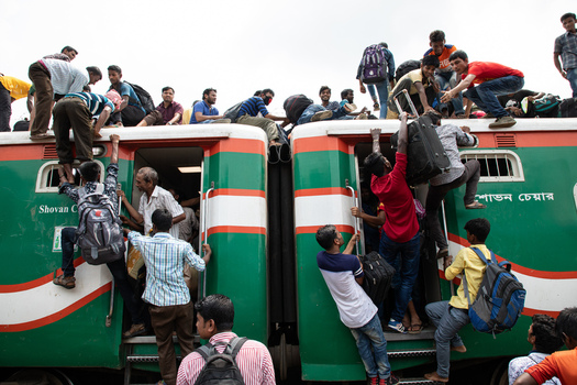 Dhaka Bangladesh 14 June 2018 View of crowds of passengers climbing onto the roof and hanging from the doors of a green and orange train at Airport Railway Station. Dhaka Bangladesh 14 June 2018 View of crowds of passengers climbing onto the roof and hanging from the doors of a green and orange train at Airport Railway Station.
