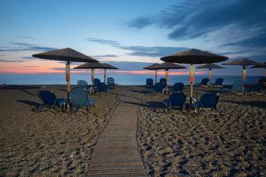 View of beach chairs and umbrellas dotting the sandy shore under the pastel hues of the early morning sky Kathisma Lefkada Greece. View of beach chairs and umbrellas dotting the sandy shore under the pastel hues of the early morning sky Kathisma Lefkada Greece.