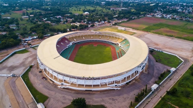 Aerial view of a large circular stadium featuring a green pitch and running track surrounded by lush greenery and urban landscape in Ghana. Aerial view of a large circular stadium featuring a green pitch and running track surrounded by lush greenery and urban landscape in Ghana.