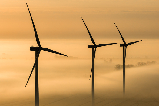 Aerial view of wind turbines piercing through a dense fog their stark silhouettes contrasting against the soft golden light of dawn Wislina Pomeranian Voivodeship Poland. Aerial view of wind turbines piercing through a dense fog their stark silhouettes contrasting against the soft golden light of dawn Wislina Pomeranian Voivodeship Poland.
