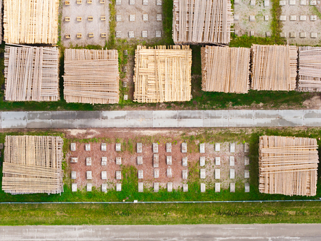 Aerial view of stacked lumber and timber logs arranged in a forestry yard with concrete foundations and surrounding green grass Latvia. Aerial view of stacked lumber and timber logs arranged in a forestry yard with concrete foundations and surrounding green grass Latvia.