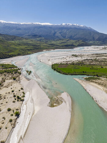 Aerial view of Vjosa Wild River National Park with turquoise river waters expansive gravel banks and snow capped mountains in the background near Permet Gjirokaster County Albania. Aerial view of Vjosa Wild River National Park with turquoise river waters expansive gravel banks and snow capped mountains in the background near Permet Gjirokaster County Albania.