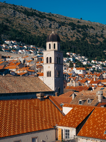 View of the historic bell tower of the Franciscan Monastery rising above terracotta rooftops with a rocky hillside in the background Dubrovnik Dubrovnik Neretva County Croatia. View of the historic bell tower of the Franciscan Monastery rising above terracotta rooftops with a rocky hillside in the background Dubrovnik Dubrovnik Neretva County Croatia.