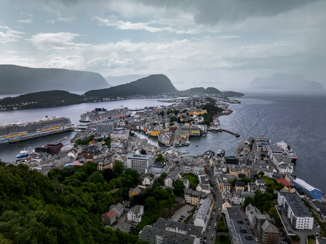 Aerial view of the coastal town of Alesund with Art Nouveau architecture cruise ships in the harbor and surrounding mountains under a cloudy sky in Alesund More og Romsdal Norway. Aerial view of the coastal town of Alesund with Art Nouveau architecture cruise ships in the harbor and surrounding mountains under a cloudy sky in Alesund More og Romsdal Norway.