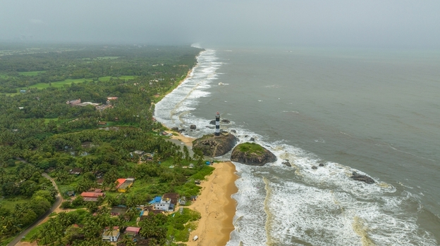 Aerial view of Kapu Light House standing on rocky outcrops surrounded by crashing waves sandy beaches and lush tropical vegetation along the coastline in Udupi Karnataka India.