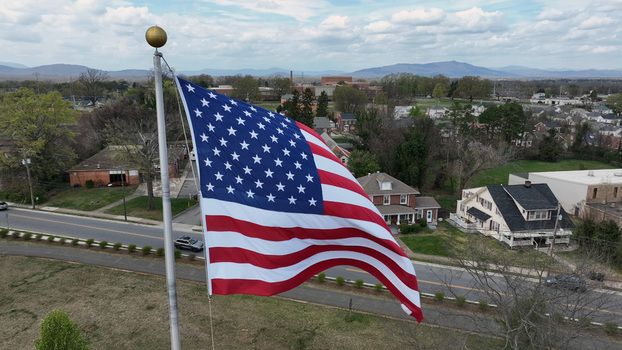 Aerial view of a large American flag waving on a flagpole above a residential neighborhood with houses roads and distant mountains in Lynchburg Virginia United States.
