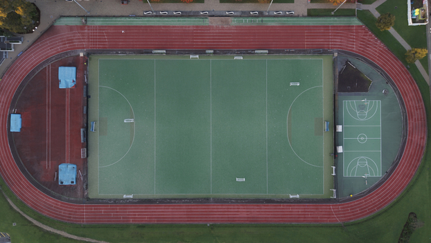 Aerial view of a sports complex featuring a green hockey pitch a red running track and a basketball court in Melbourne Victoria Australia.