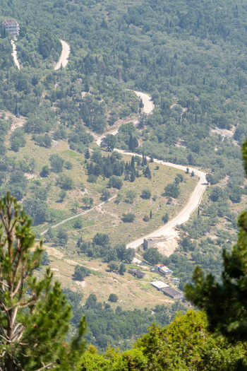 View of a winding mountain road through dense green forest and hills at Panorama Llogora in Himare Qarku i Vlores Albania.