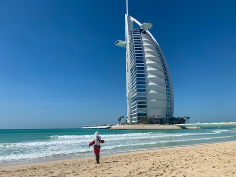 View of Burj Al Arab hotel with a lifeguard in red shorts standing on the sandy beach by the turquoise sea under a clear blue sky in Dubai Dubai United Arab Emirates. View of Burj Al Arab hotel with a lifeguard in red shorts standing on the sandy beach by the turquoise sea under a clear blue sky in Dubai Dubai United Arab Emirates.