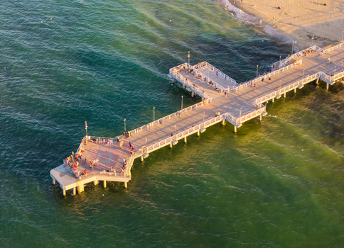 Aerial view of Brzezno pier extending into the Baltic Sea with people walking on the wooden deck during golden hour in Gdansk Pomeranian Voivodeship Poland. Aerial view of Brzezno pier extending into the Baltic Sea with people walking on the wooden deck during golden hour in Gdansk Pomeranian Voivodeship Poland.