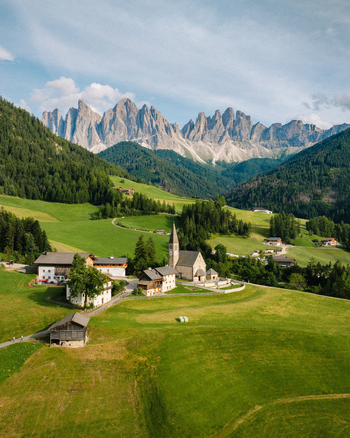 Aerial view of Chiesa di Santa Maddalena surrounded by lush green meadows and the jagged peaks of the Odle Group in Santa Maddalena Alta Trentino Alto Adige Italy.