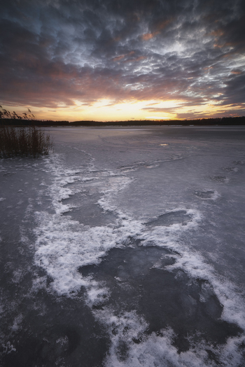 View of a frozen lake with ice patterns and snow under a dramatic sunset sky with orange clouds Gorzyce Silesian Voivodeship Poland.