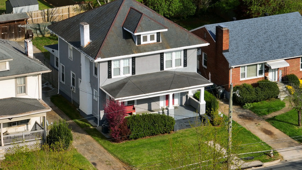 Aerial view of a gray residential house with a front porch green lawn and surrounding suburban homes in Lynchburg Virginia United States.