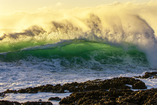 View of a large ocean wave crashing against the rocky shore of the North Shore during golden hour in Haleiwa Hawaii United States.