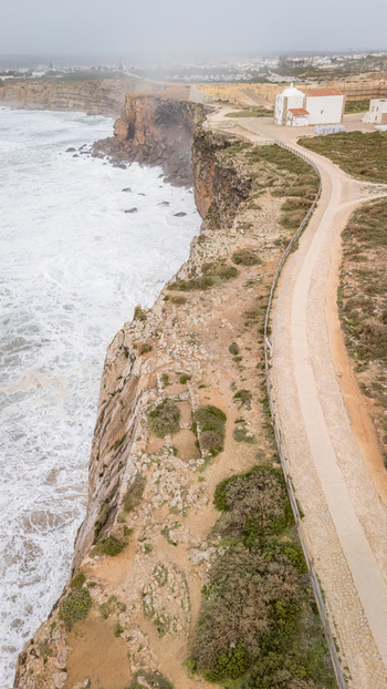 Aerial view of Sagres Fortress on the edge of steep cliffs overlooking the Atlantic Ocean with crashing waves and a misty horizon in Sagres Faro Portugal. Aerial view of Sagres Fortress on the edge of steep cliffs overlooking the Atlantic Ocean with crashing waves and a misty horizon in Sagres Faro Portugal.