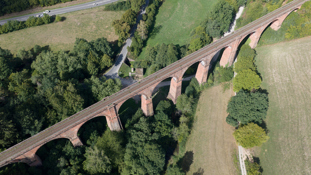 Aerial view of Himbachel Viadukt a historic red brick railway bridge surrounded by lush green forests and agricultural fields in Erbach Hessen Germany. Aerial view of Himbachel Viadukt a historic red brick railway bridge surrounded by lush green forests and agricultural fields in Erbach Hessen Germany.
