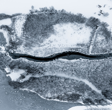 Aerial view of a winding river cutting through a snow covered forest landscape in Latvia. Aerial view of a winding river cutting through a snow covered forest landscape in Latvia.