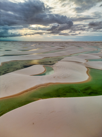 Aerial view of Lagoa Bonita featuring white sand dunes and vibrant green rainwater lagoons under a dramatic cloudy sky in Barreirinhas State of Maranhao Brazil. Aerial view of Lagoa Bonita featuring white sand dunes and vibrant green rainwater lagoons under a dramatic cloudy sky in Barreirinhas State of Maranhao Brazil.