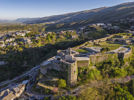 Aerial view of Gjirokaster Fortress on a rocky hill overlooking the historic town with stone rooftops and lush green surroundings in Gjirokaster Gjirokaster County Albania. Aerial view of Gjirokaster Fortress on a rocky hill overlooking the historic town with stone rooftops and lush green surroundings in Gjirokaster Gjirokaster County Albania.