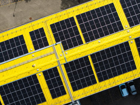 Aerial view of a bright yellow industrial roof covered with solar panels and parked cars below in Valdlauci Kekava Municipality Latvia. Aerial view of a bright yellow industrial roof covered with solar panels and parked cars below in Valdlauci Kekava Municipality Latvia.