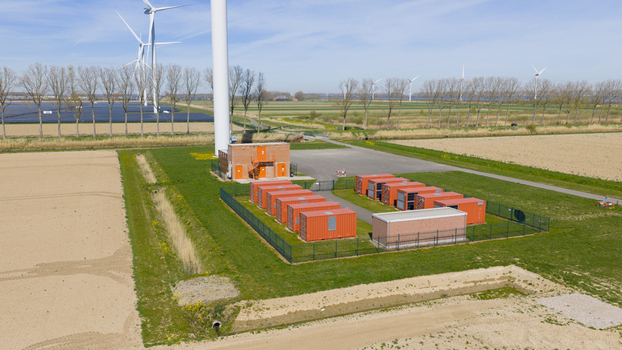 Aerial view of Energiepark Haringvliet Zuid featuring wind turbines and orange battery storage containers surrounded by green fields in Middelharnis South Holland Netherlands.