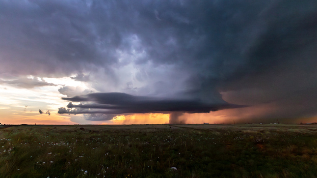 View of a dramatic supercell thunderstorm with dark swirling clouds and rain curtains over the flat plains during sunset in Oklahoma City Oklahoma United States.