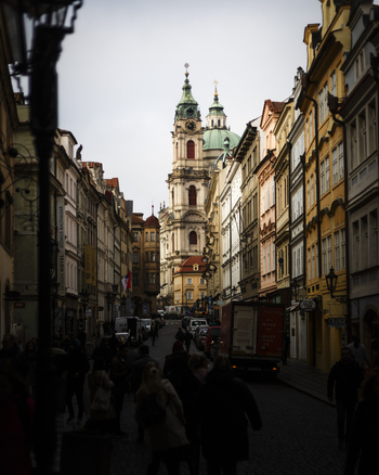 Prague Czechia 25 November 2022 View of St. Nicholas Church at the end of a narrow street lined with colorful historic buildings and people walking in Mala Strana.