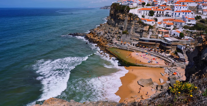 Aerial view of Azenhas do Mar a coastal village with white houses perched on cliffs above the Atlantic Ocean featuring a natural swimming pool and sandy beach in Colares Lisbon Portugal. Aerial view of Azenhas do Mar a coastal village with white houses perched on cliffs above the Atlantic Ocean featuring a natural swimming pool and sandy beach in Colares Lisbon Portugal.