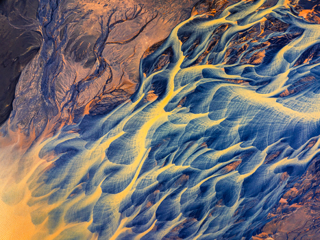 Aerial view of a glacial river delta with intricate blue and yellow sediment patterns flowing through volcanic terrain in Iceland. Aerial view of a glacial river delta with intricate blue and yellow sediment patterns flowing through volcanic terrain in Iceland.