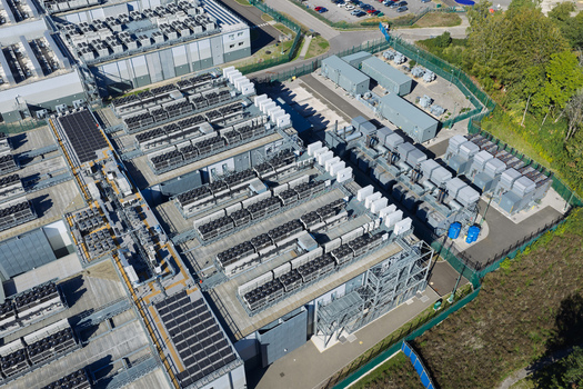 Aerial view of a large data center facility featuring rows of industrial cooling units complex HVAC infrastructure and a secure fenced perimeter in the United Kingdom.