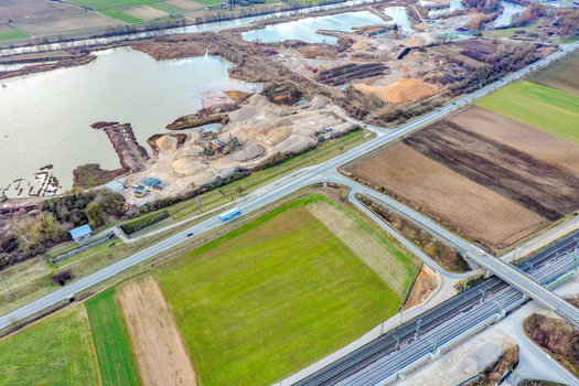 Aerial view of a gravel quarry with sand piles and heavy machinery next to a river and railway tracks in a rural landscape Buttenheim Bavaria Germany. Aerial view of a gravel quarry with sand piles and heavy machinery next to a river and railway tracks in a rural landscape Buttenheim Bavaria Germany.